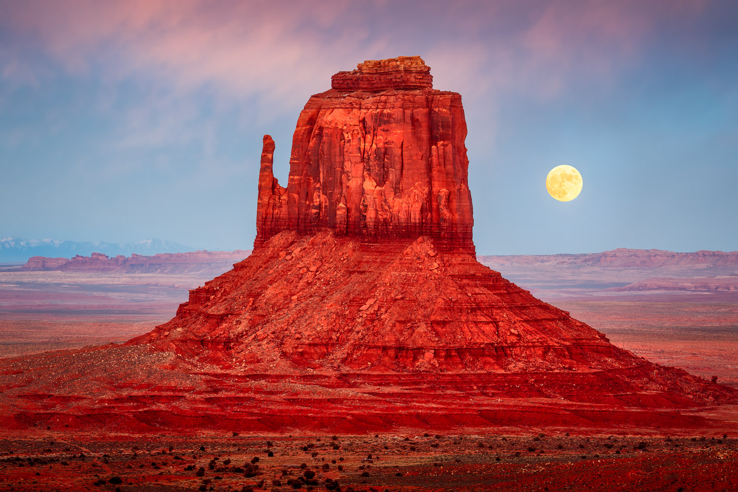 A full moon rising over a red rock butte in the desert of monument valley Arizona.